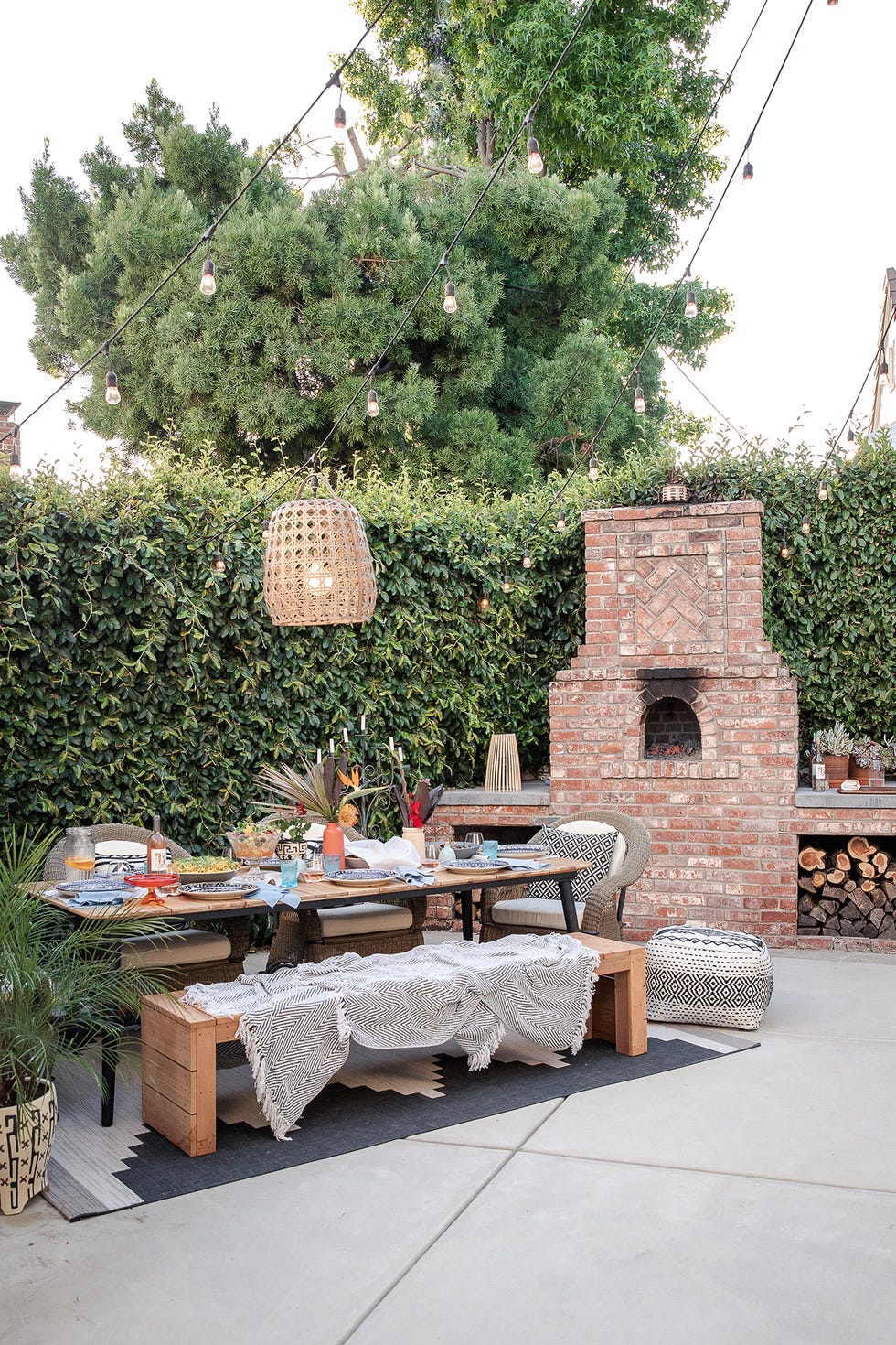 comedor exterior con mesa de madera, un banco, barbacoa de obra, guirnaldas de luces y una lámpara de fibras