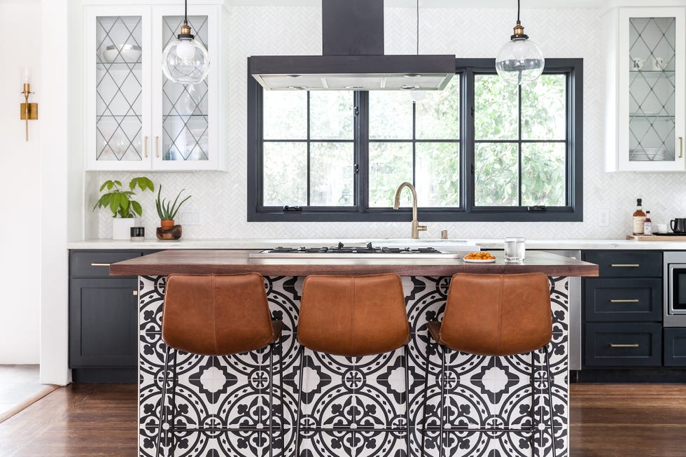 cocina moderna con isla central revestida con azulejos y tres taburetes de piel marrón