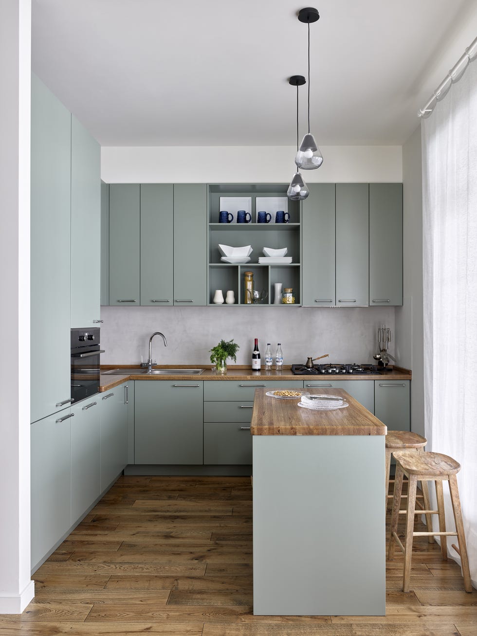 cocina abierta con isla central, armarios de color verde empolvado y encimeras de madera