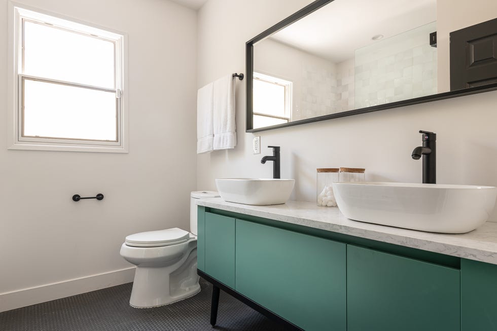 baño con mueble bajolavabo moderno con puertas sin tiradores en color verde, encimera de mármol y dos lavabos con grifos de color negro mate