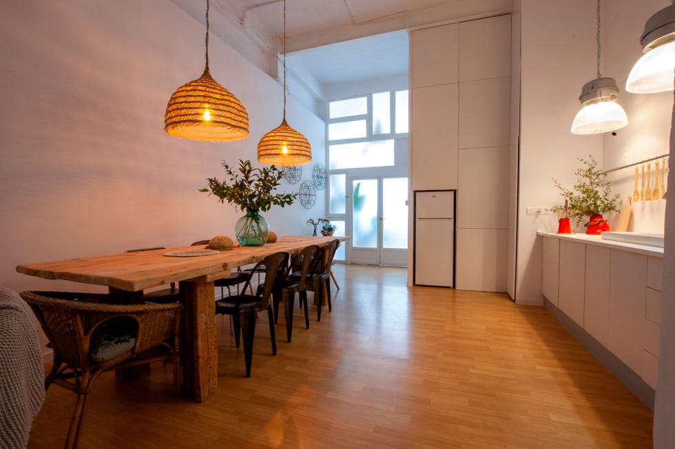 comedor abierto a la cocina con mesa de madera raw, sillas de metal y lámparas de fibras