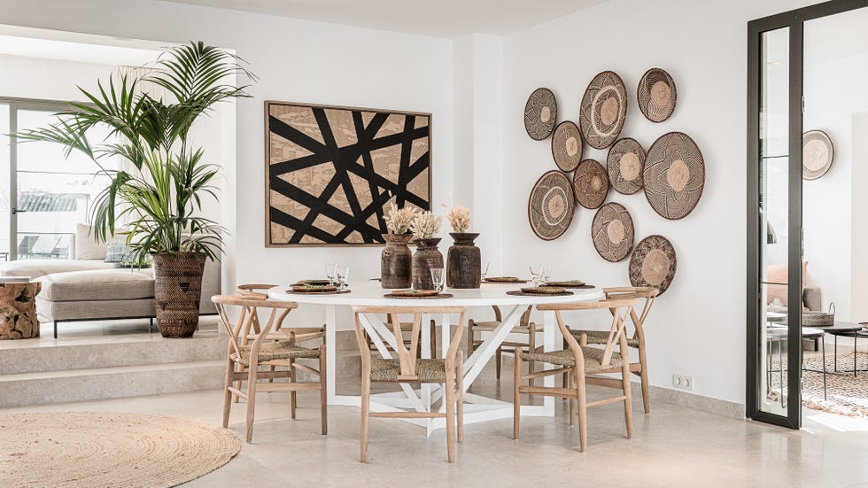 comedor con mesa redonda blanca, sillas de fibras naturales, plantas y cestos decorativos en la pared