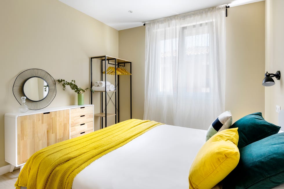dormitorio moderno decorado con detalles mostaza, aparador de madera mid century, y pequeño vestidor abierto