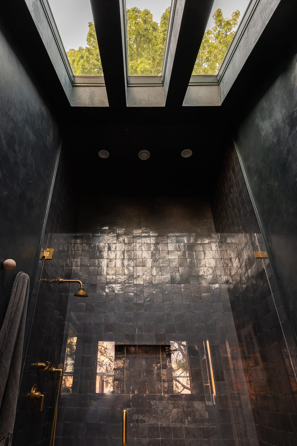 ducha con azulejos negros y grifería de latón y tragaluz