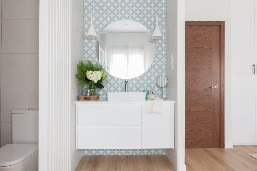 baño en suite con mueble volado blanco, papel con motivos geométricos y espejo redondo