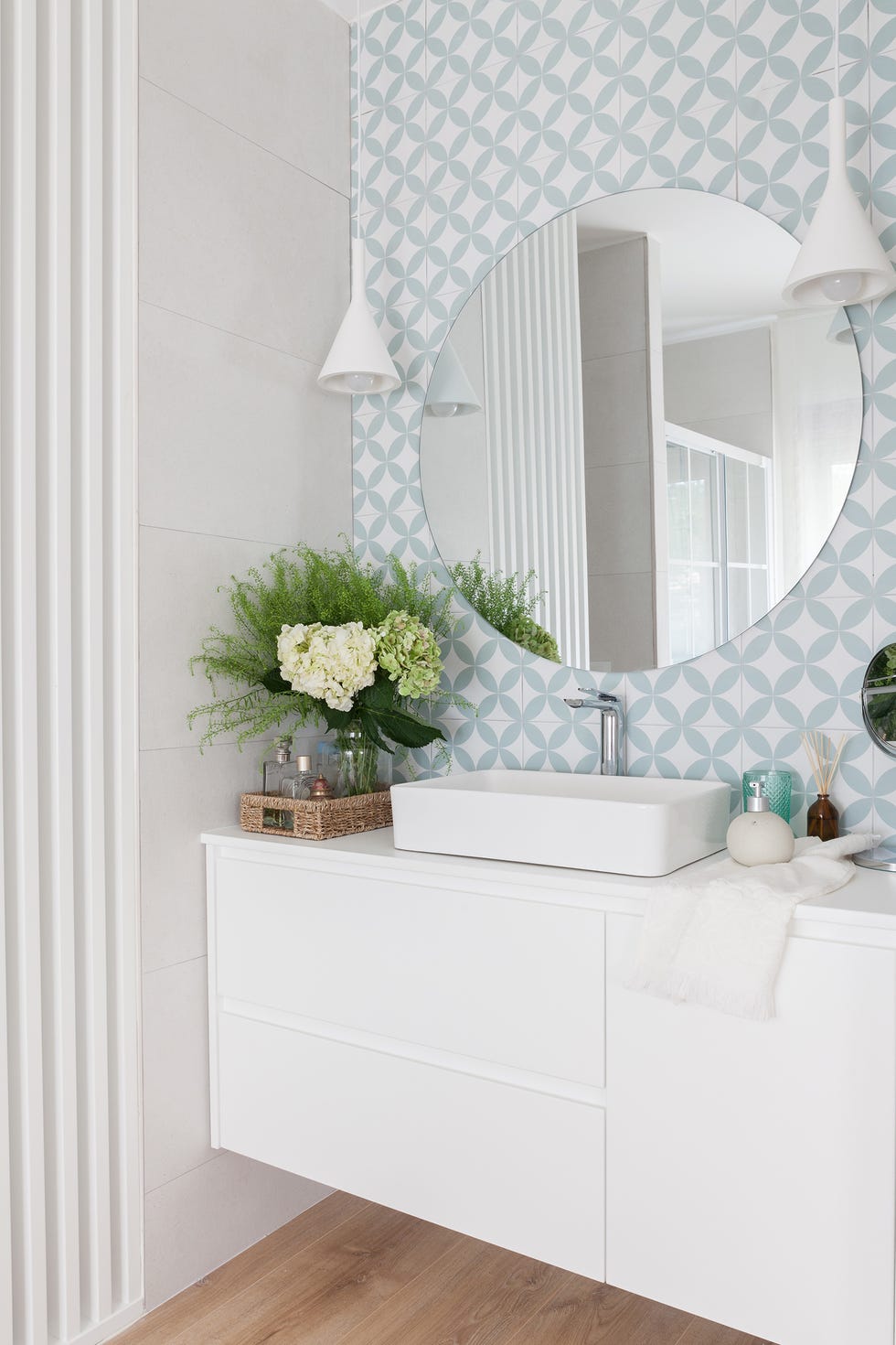 baño en suite con mueble volado blanco, papel con motivos geométricos y espejo redondo