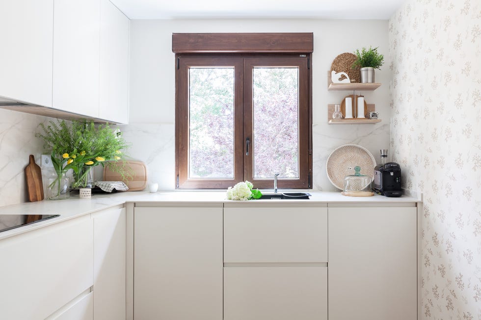 cocina con armarios blancos con acabado mate sin tiradores, revestimiento efecto mármol y pared con papel pintado con motivos botánicos