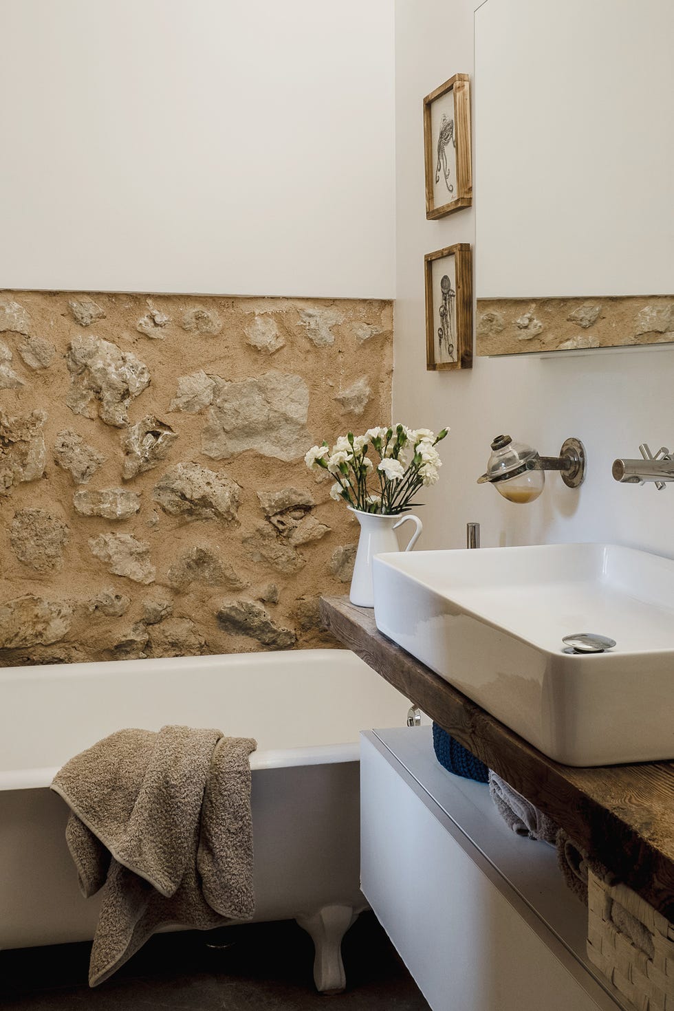 baño rústico con bañera y pared de piedra vista