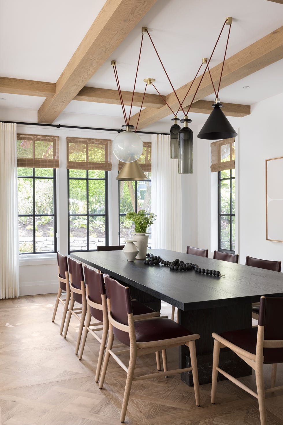 mesa de comedor de madera, sillas de piel burdeos y lámpara suspendida de latón