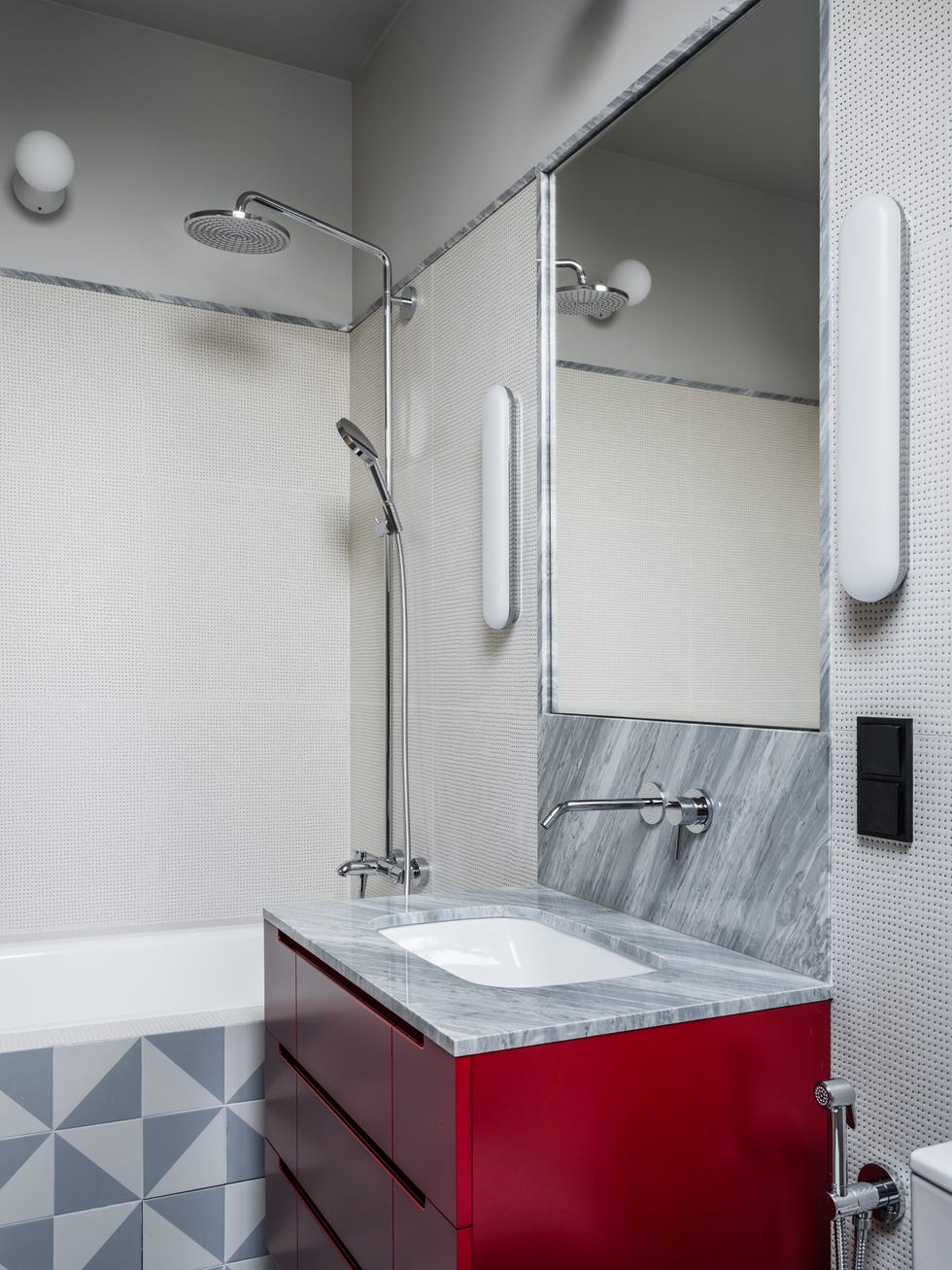 baño con azulejos geométricos y mueble suspendido en color rojo con encimera de mármol
