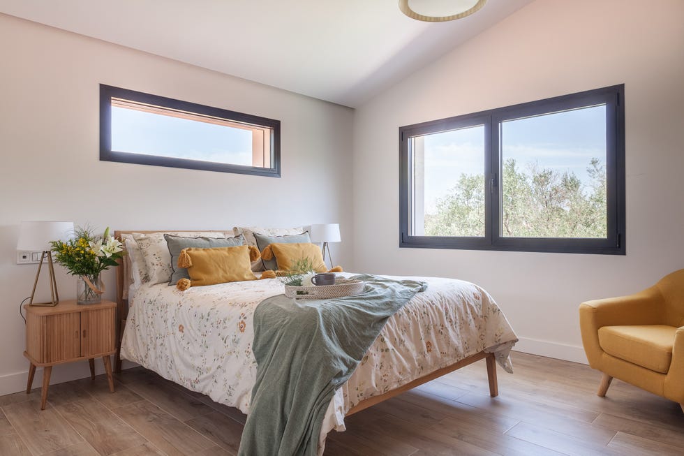 dormitorio con cama y dos mesillas de madera y butaca mostaza