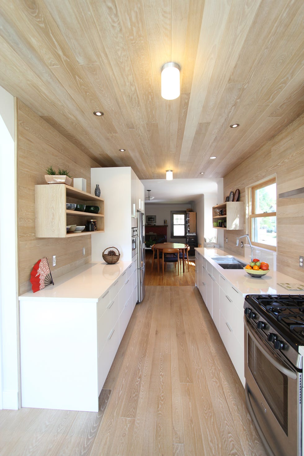 cocina moderna abierta con armarios blancos y suelos, techos y paredes de madera