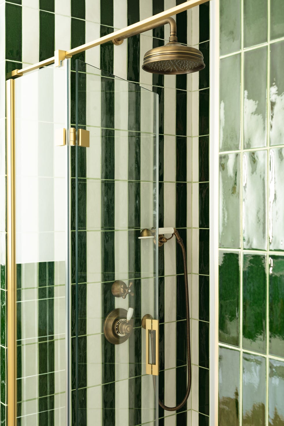 ducha con azulejos verdes y blancos y grifo dorado