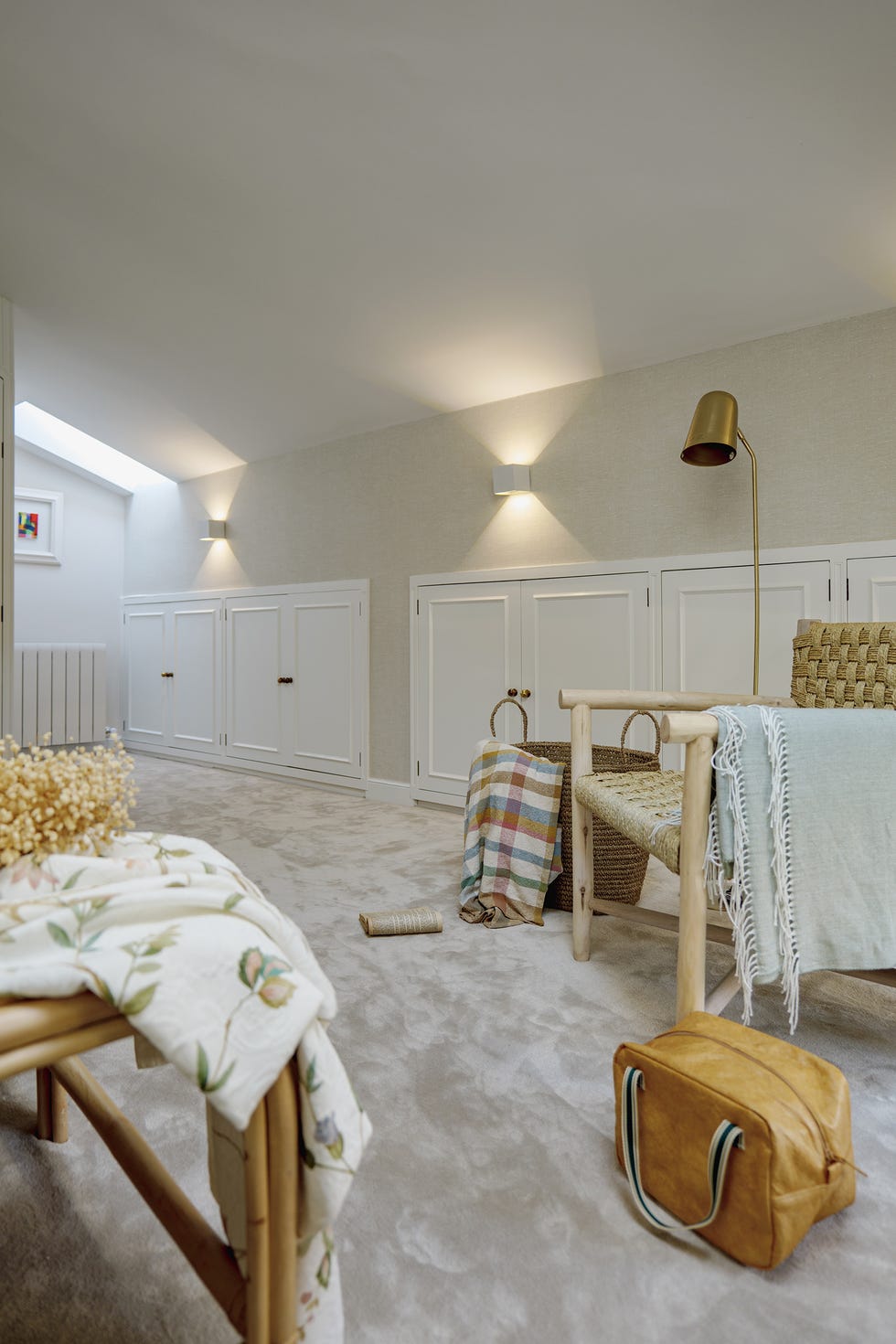 dormitorio con moqueta beige, butaca de ratán y papel pintado con efecto tejido