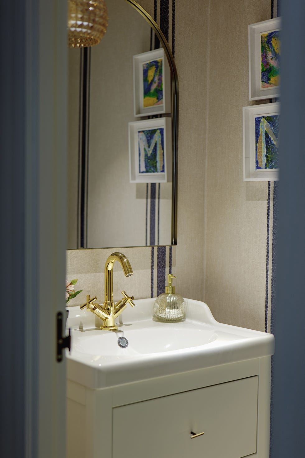 aseo con mueble blanco, grifo dorado y papel pintado a rayas azules