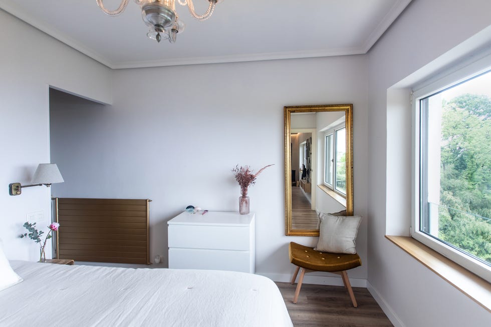 dormitorio decorado en blanco con espejo de pared con el marco dorado