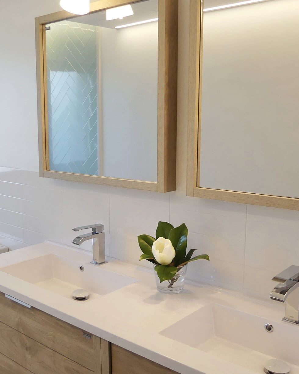 baño decorado en blanco con mueble de madera bajo lavabo a juego con el marco de los espejos