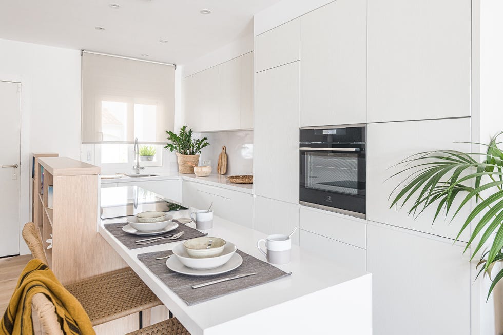 cocina abierta diseñada en blanco con barra de desayunos y taburetes de fibras