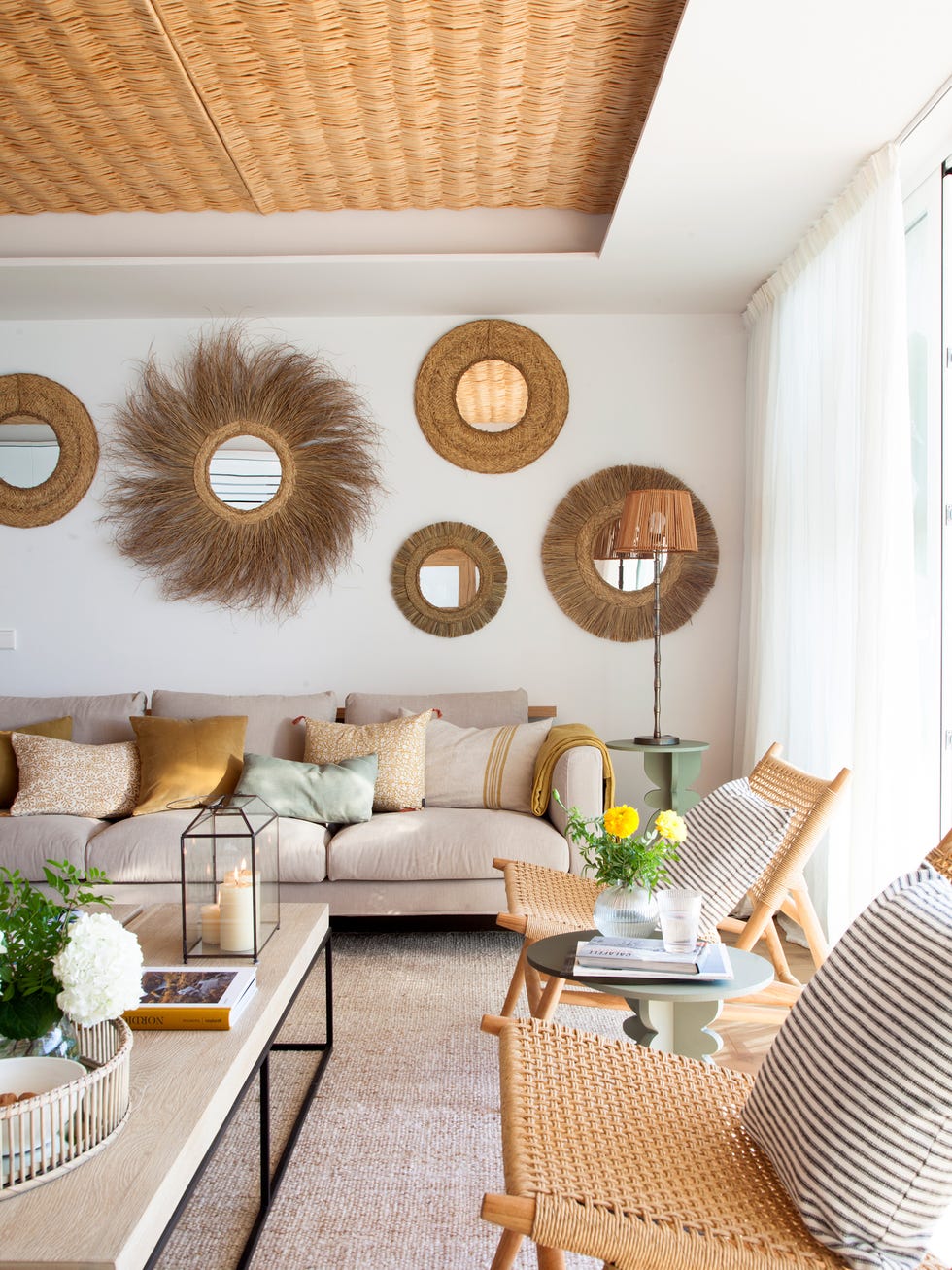 salón con sofá beige, butacas de rejilla y espejos con marcos de yute