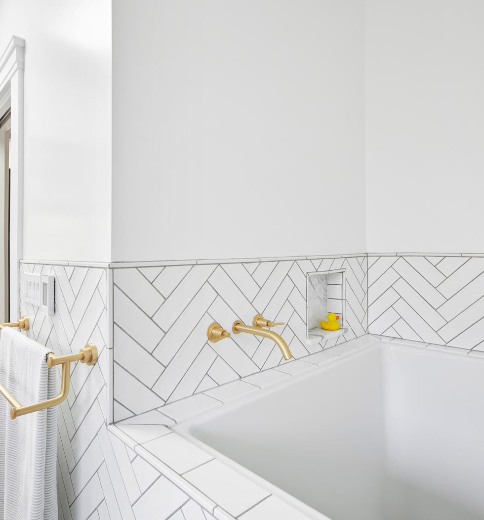 baño con bañera revestida con azulejos blancos en espiga y grifo de latón