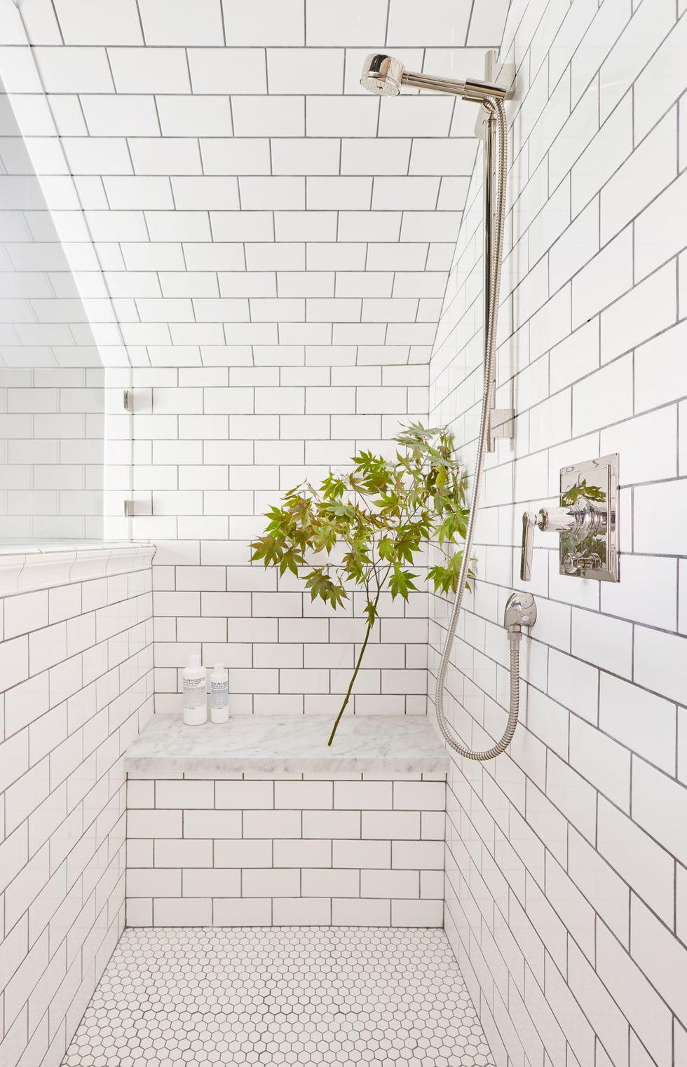 ducha revestida con azulejos tipo metro blancos y banco con balda de mármol