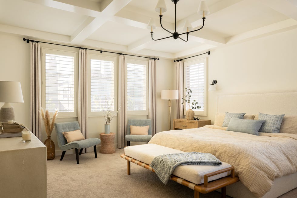 dormitorio con cama tapizada en beige, banco a los pies y dos butacas azules