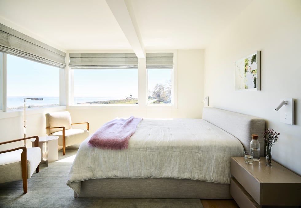dormitorio de diseño contemporáneo con cama tapizada en gris y dos butacas blancas a los pies