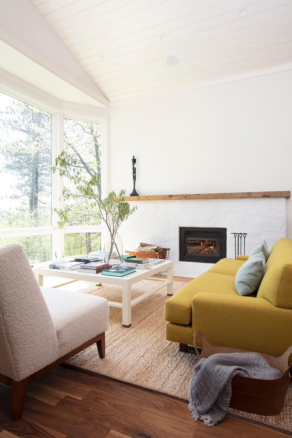 salón de diseño mid century con chimenea, sofá amarillo, butaca bouclé blanca y mesa de centro blanca sobre alfombra de fibras