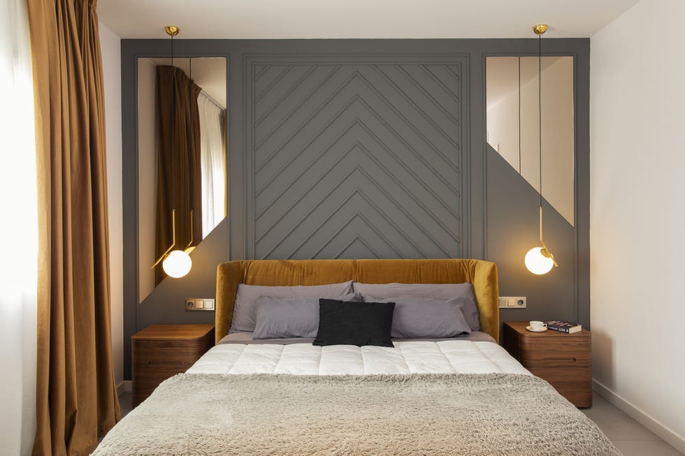 dormitorio con molduras decorativas en la pared, cabecero de terciopelo mostaza y lámparas suspendidas con bola