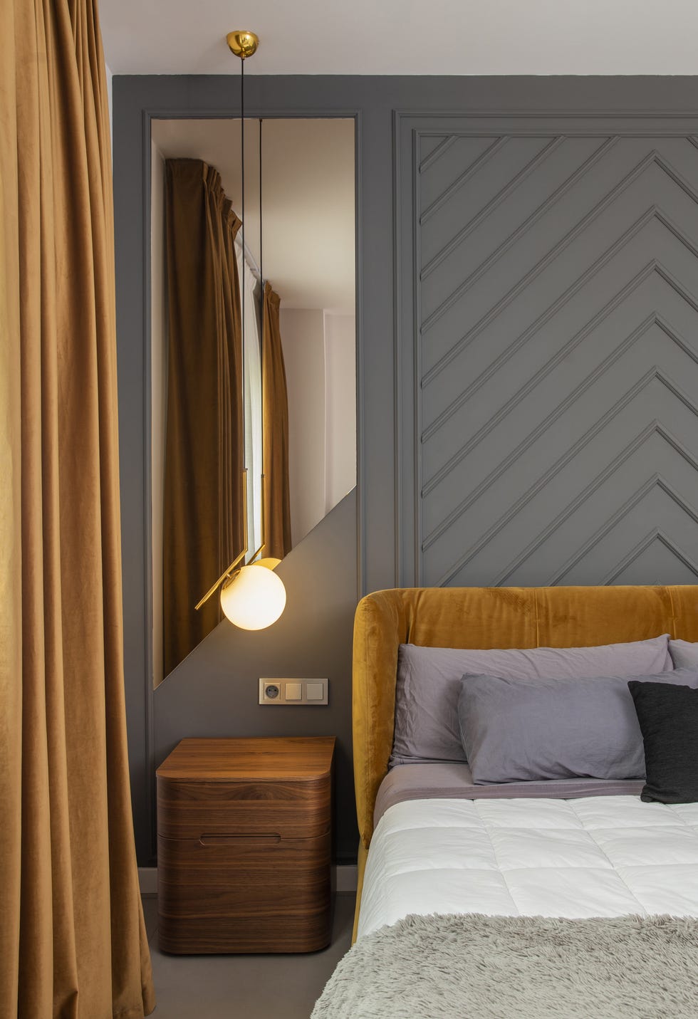dormitorio con molduras decorativas en la pared, cabecero de terciopelo mostaza y lámpara suspendidas con bola