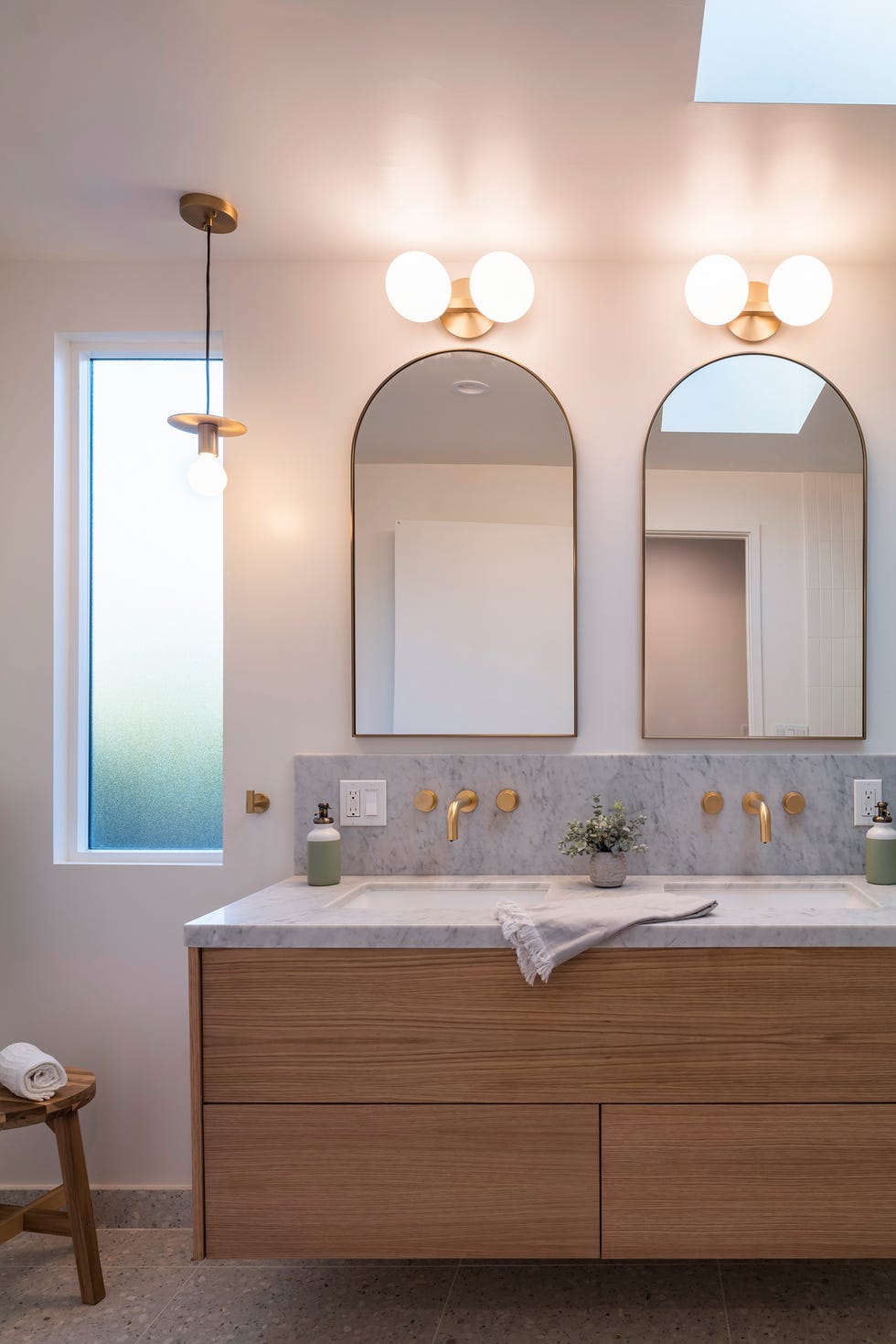 baño con mueble de madera suspendido y dos lavabos en encimera de mármol con grifos de latón