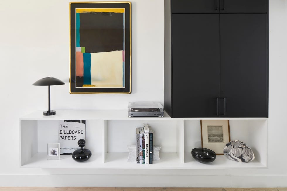 estantería blanca suspendida decorada con libros y objetos modernos, cuadro abstracto en la pared y armario con puertas metálicas negras