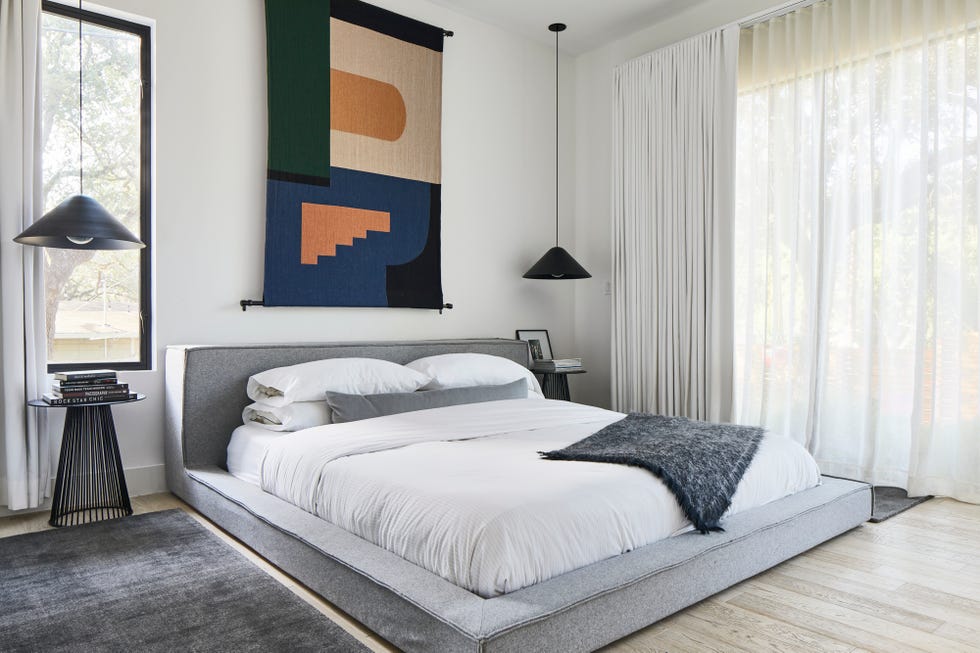 dormitorio moderno con cama tapizada en tela gris y tapiz decorativo sobre el cabecero