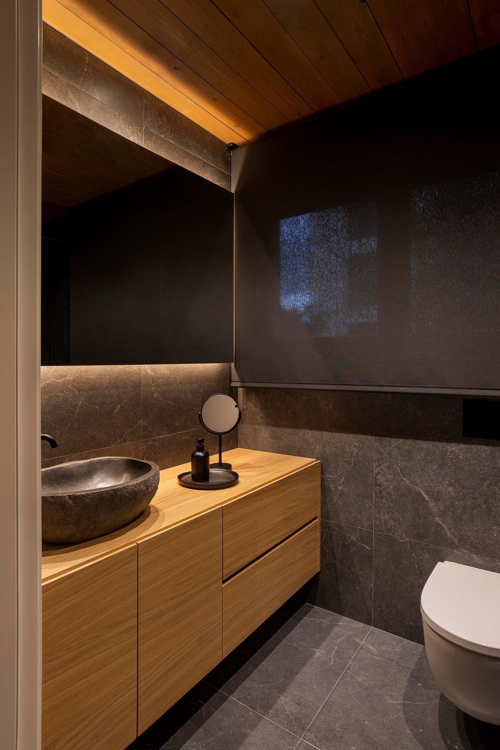 baño con mueble de madera volado y revestimientos cerámicos negros