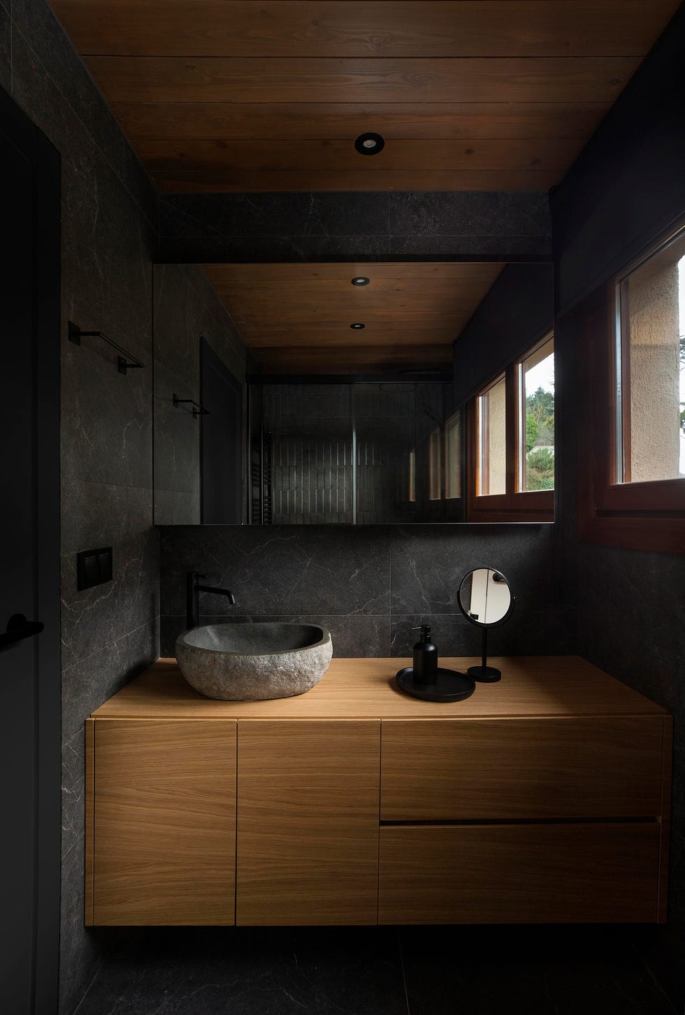 baño con mueble de madera volado y revestimientos cerámicos negros