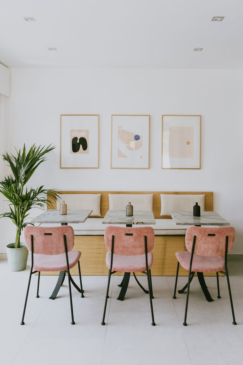 comedor con banco de madera, mesas de mármol y sillas de terciopelo rosa