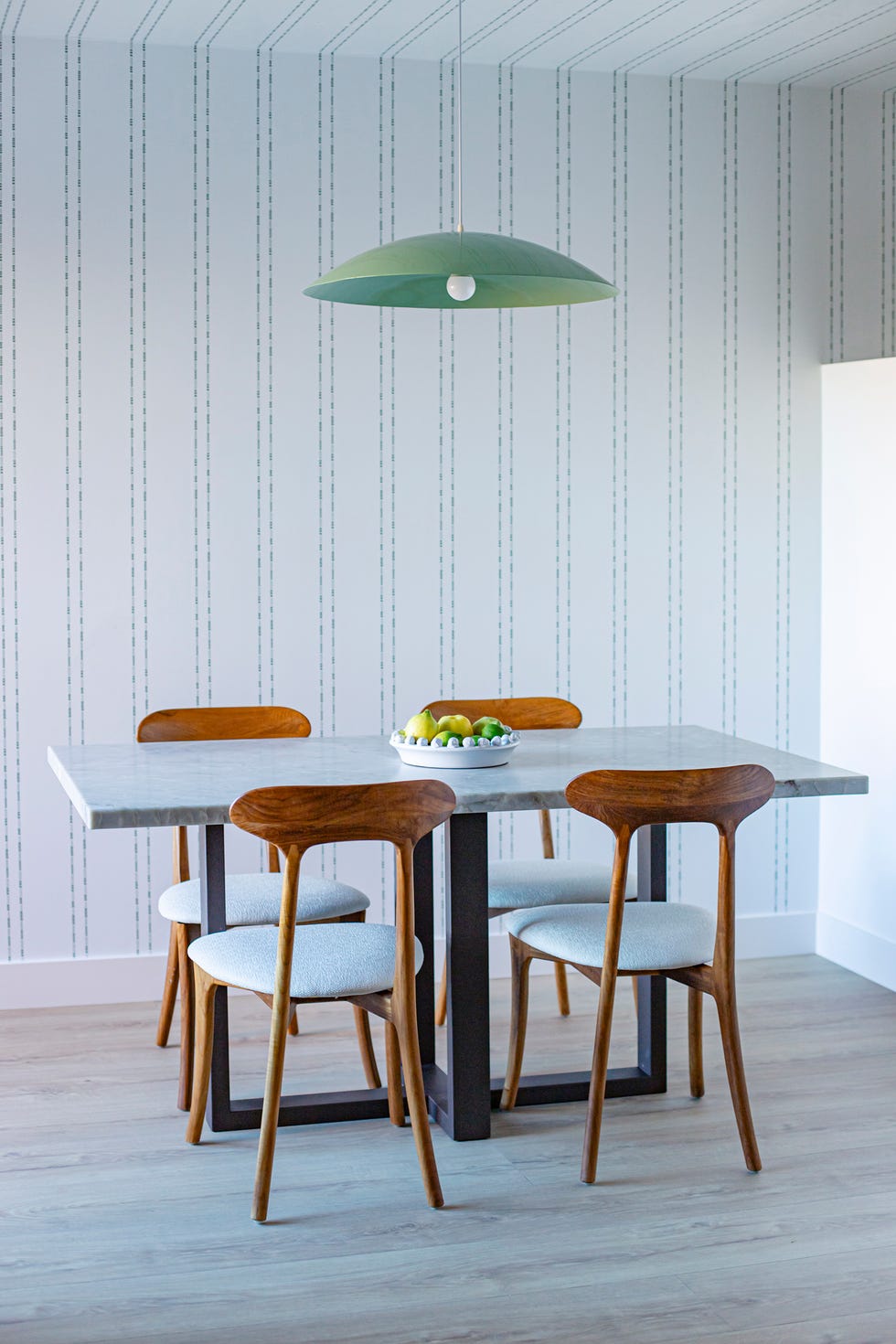 mesa de comedor con sobre de mármol, sillas de madera y lámpara suspendida con pantalla verde
