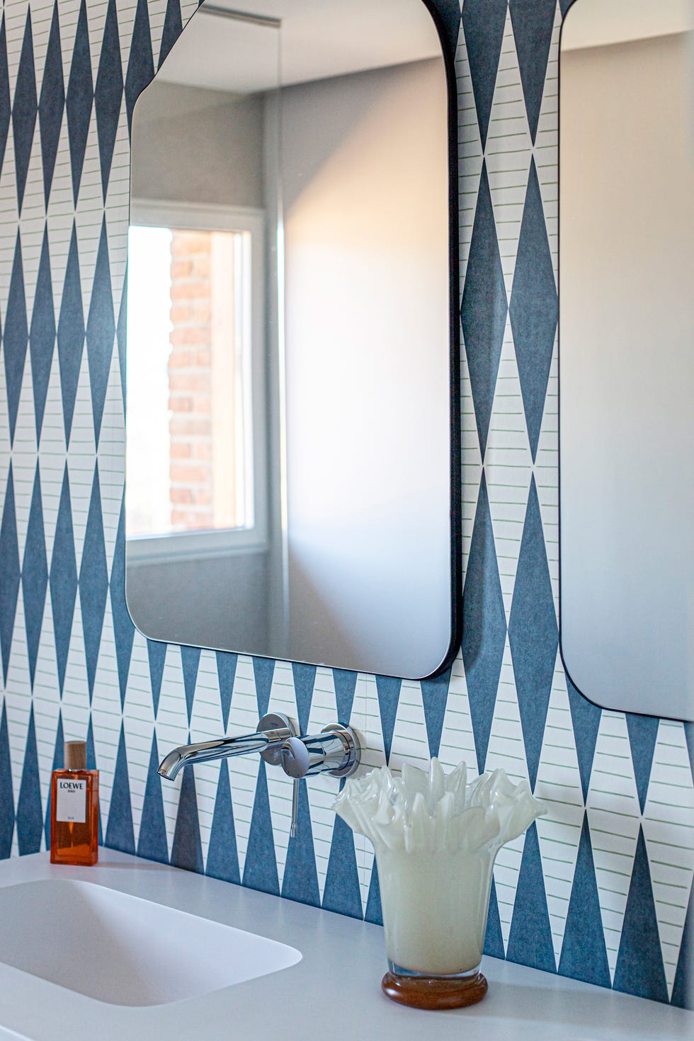 baño con papel pintado con dibujos de rombos azules y dos espejos