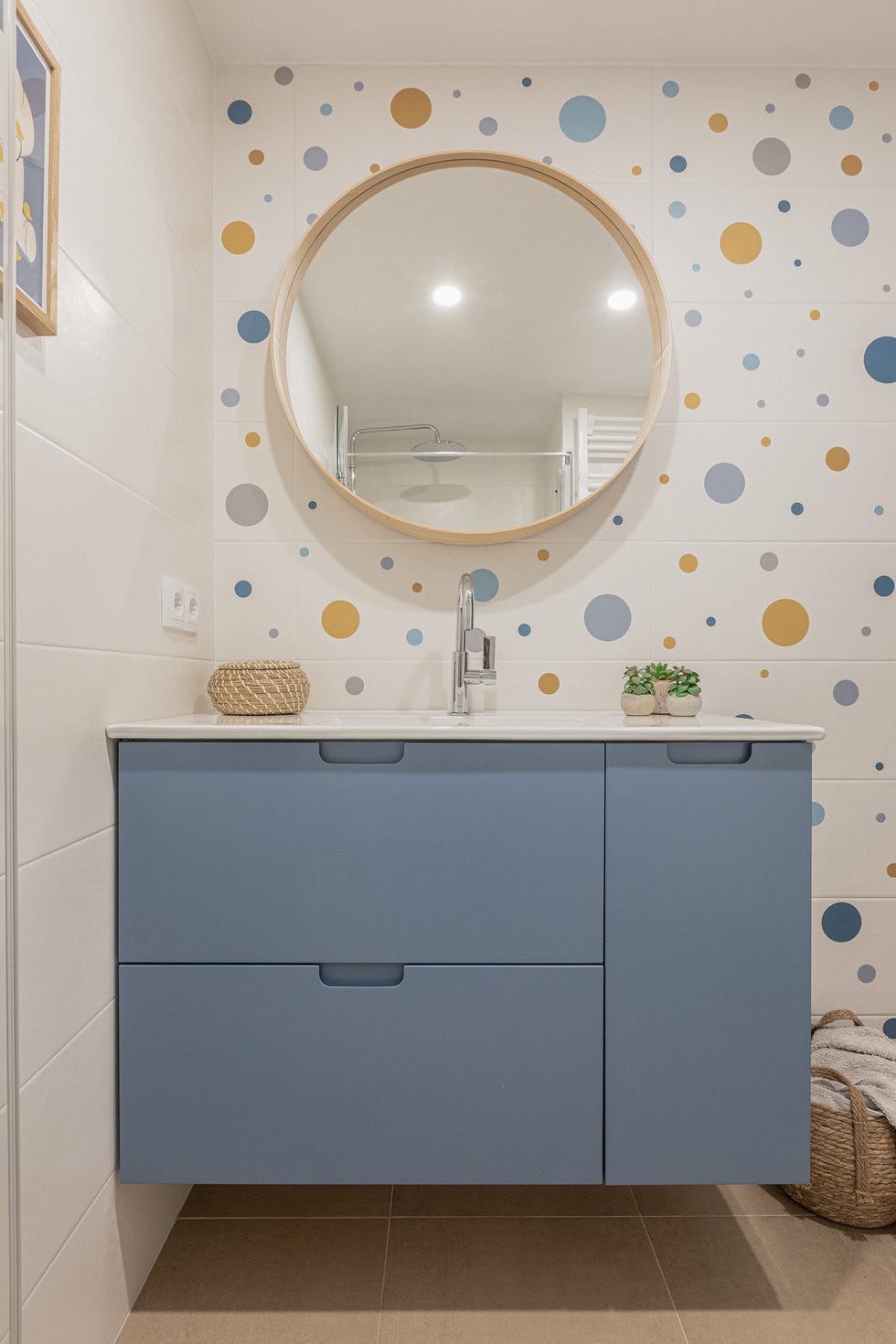 baño con mueble volado de color azul y azulejos blancos con círculos de colores