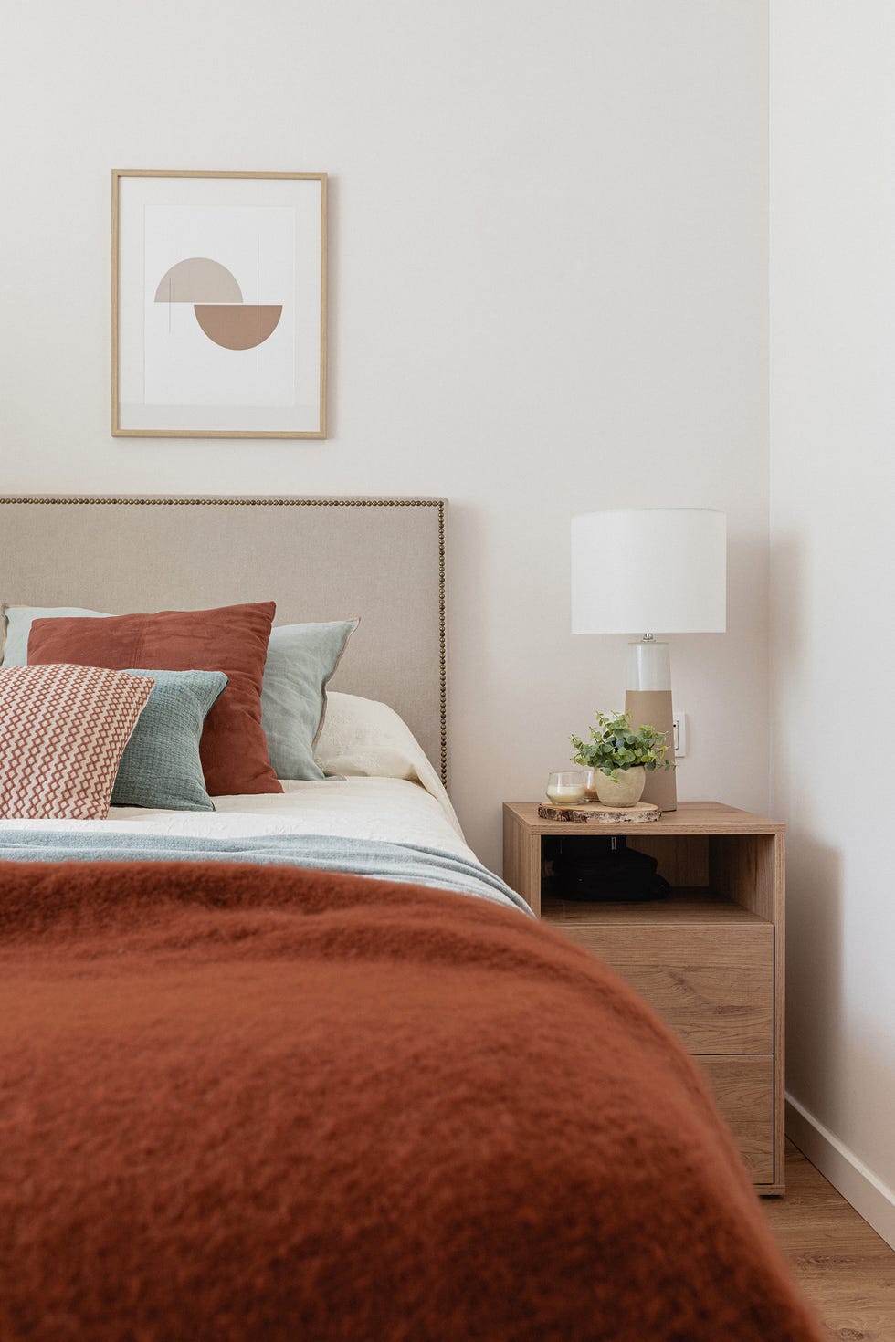 dormitorio con cabecero beige con remaches y mesita de noche de madera