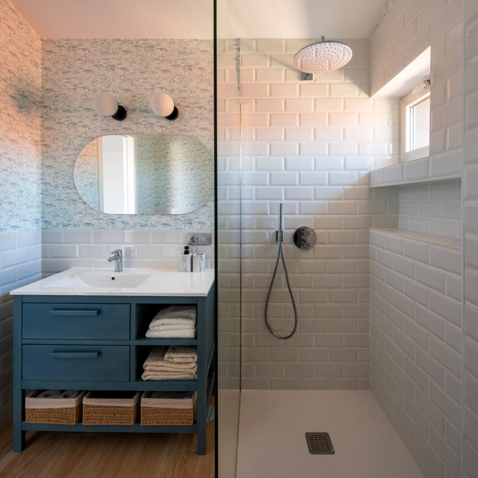 baño con ducha de obra con azulejos tipo metro en color blanco y papel pintado con peces