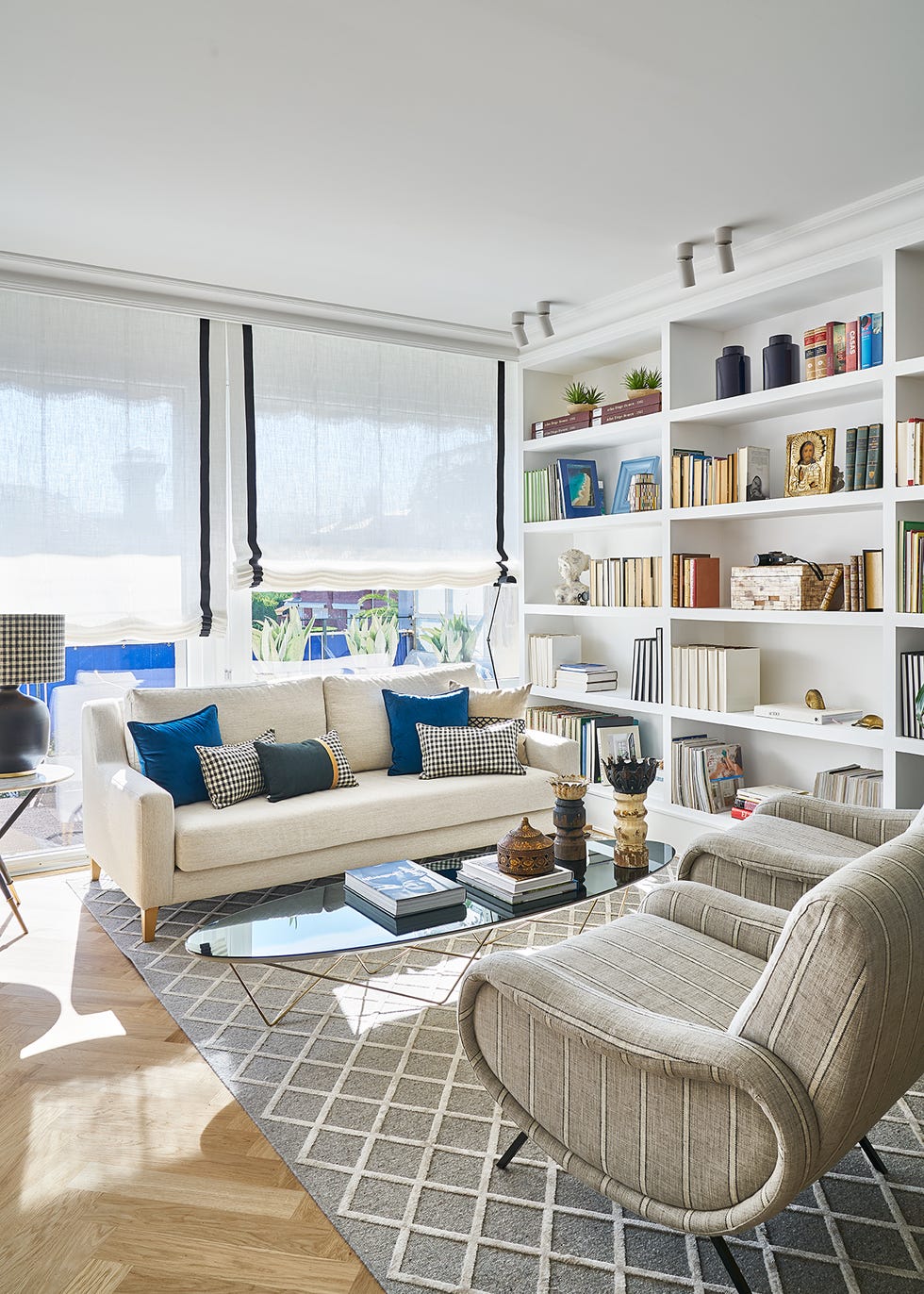 salón moderno con sofá blanco, butacas redondas tapizadas a rayas, mesa de centro con sobre de cristal negro ovalado y librería blanca a medida