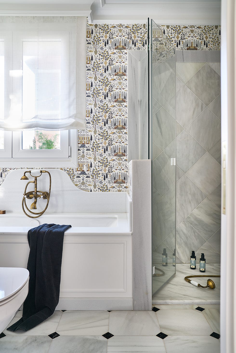 baño de estilo vintage bañera blanca, ducha revestida con mármol y papel pintado con motivos botánicos