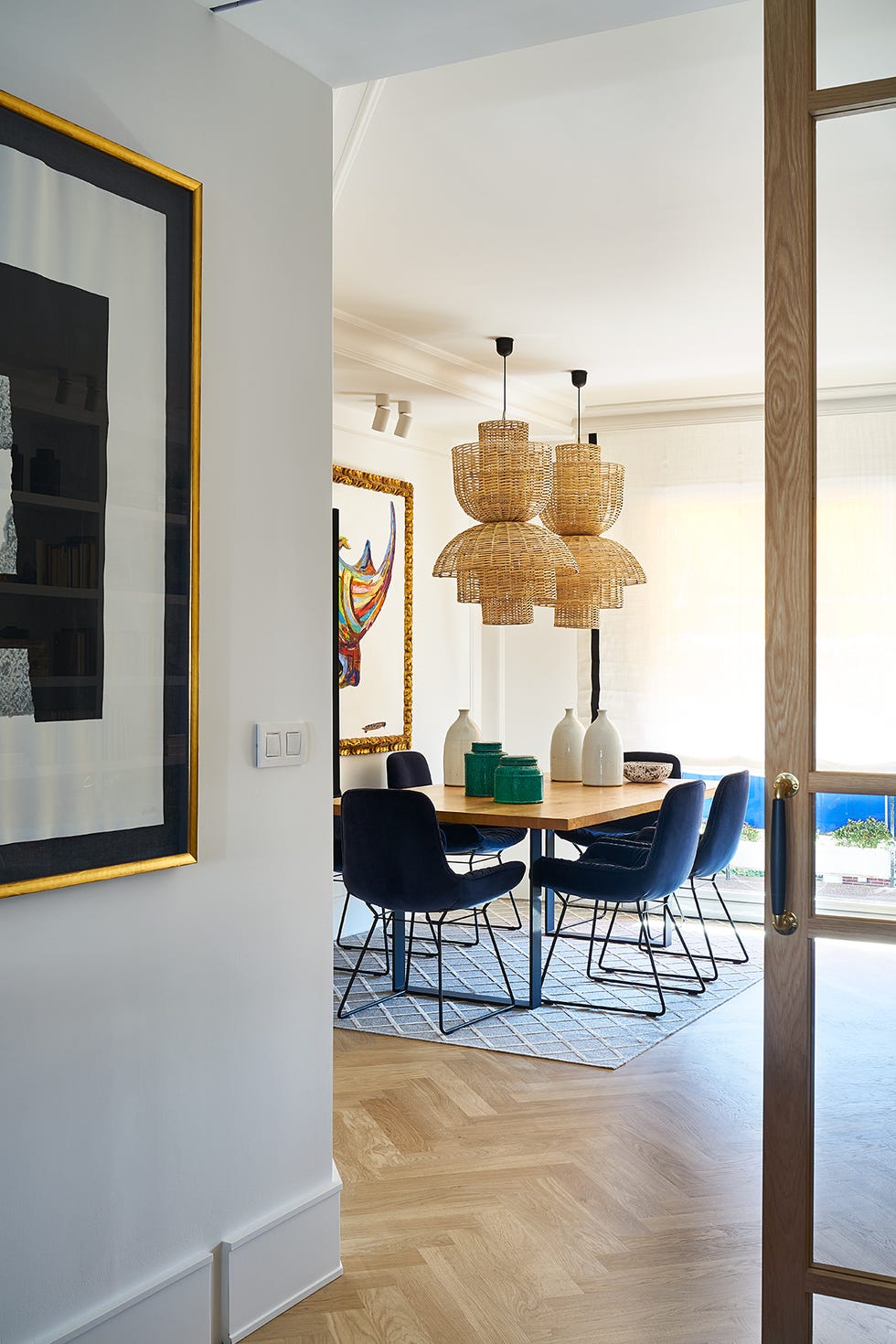 comedor con mesa de madera con patas de hierro, sillas de terciopelo azul y lámparas de techo de fibras