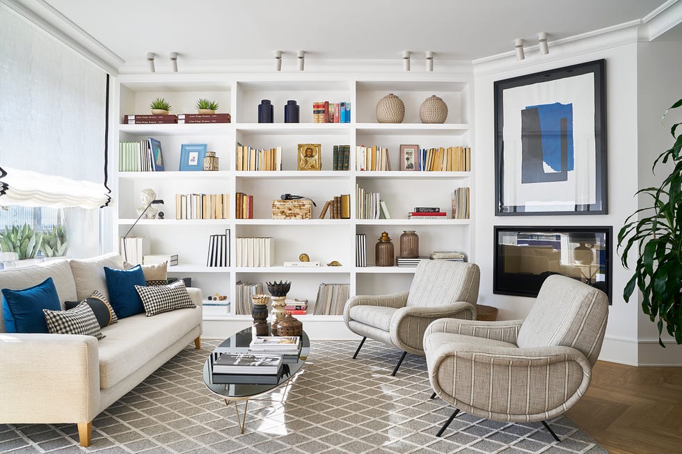 salón moderno con sofá blanco, butacas redondas tapizadas a rayas, mesa de centro con sobre de cristal negro ovalado y librería blanca a medida