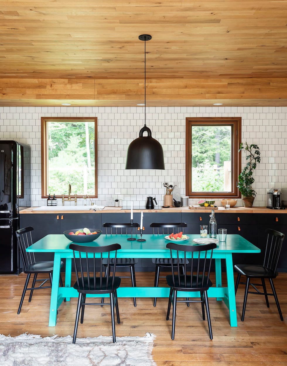 cocina rústica en blanco y negro con mesa de comedor turquesa, sillas negras y lámpara industrial de metal