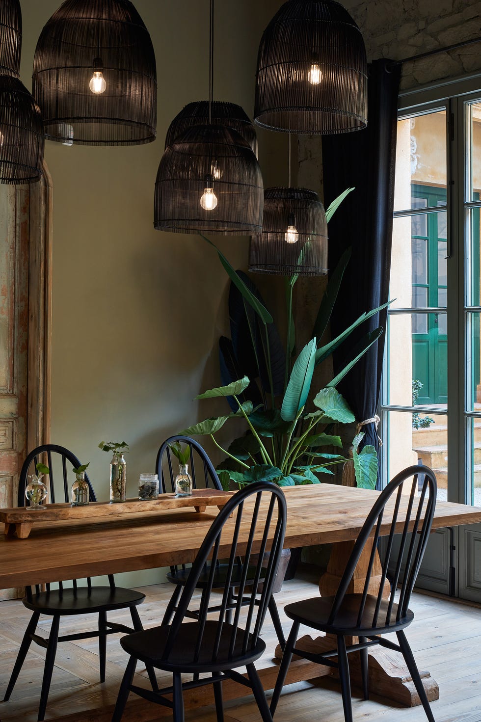 mesa de comedor de madera, sillas negras y lámparas suspendidas con pantallas tejidas en negro