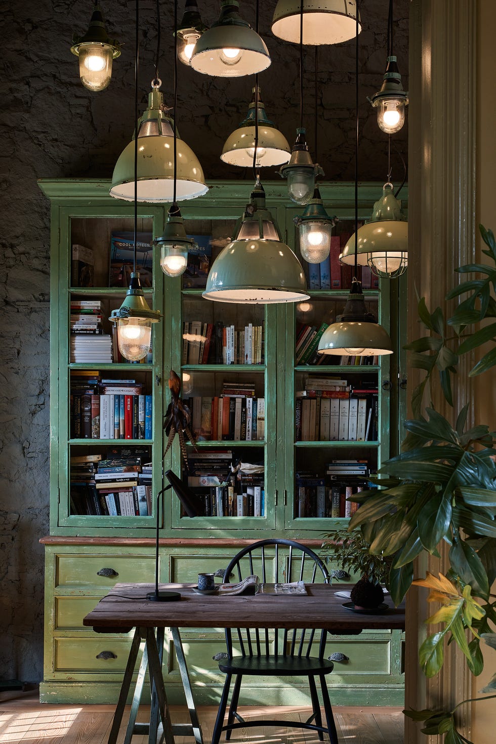 vitrina verde y mesa de escritorio de madera de estilo rústico con varias lámparas suspendidas