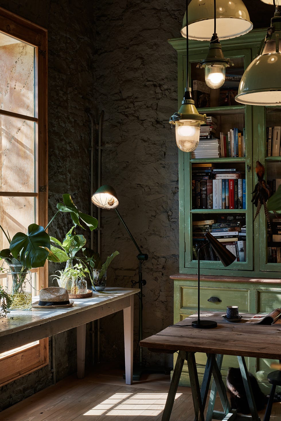 vitrina verde y mesa de escritorio de madera de estilo rústico con varias lámparas suspendidas