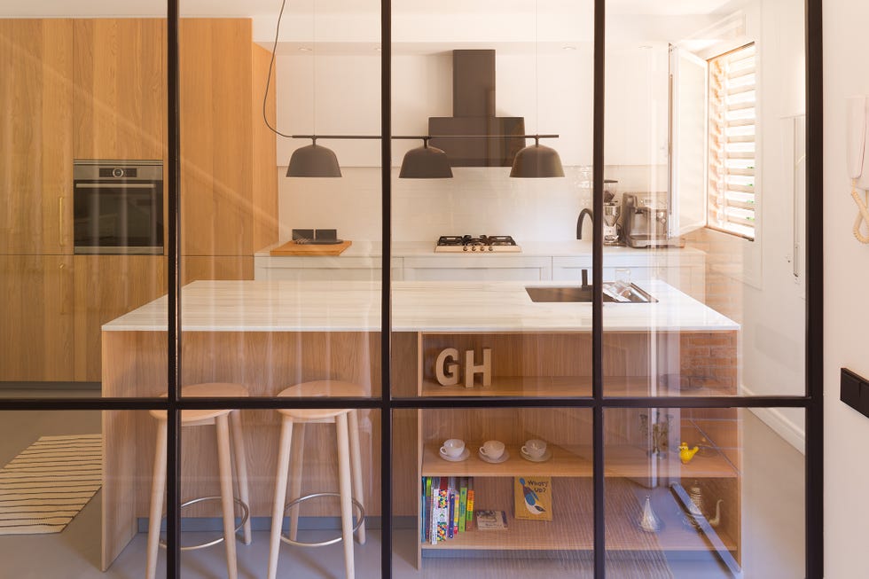 cocina moderna abierta con isla central de madera y encimera de mármol y cerramiento con perfilería metálica